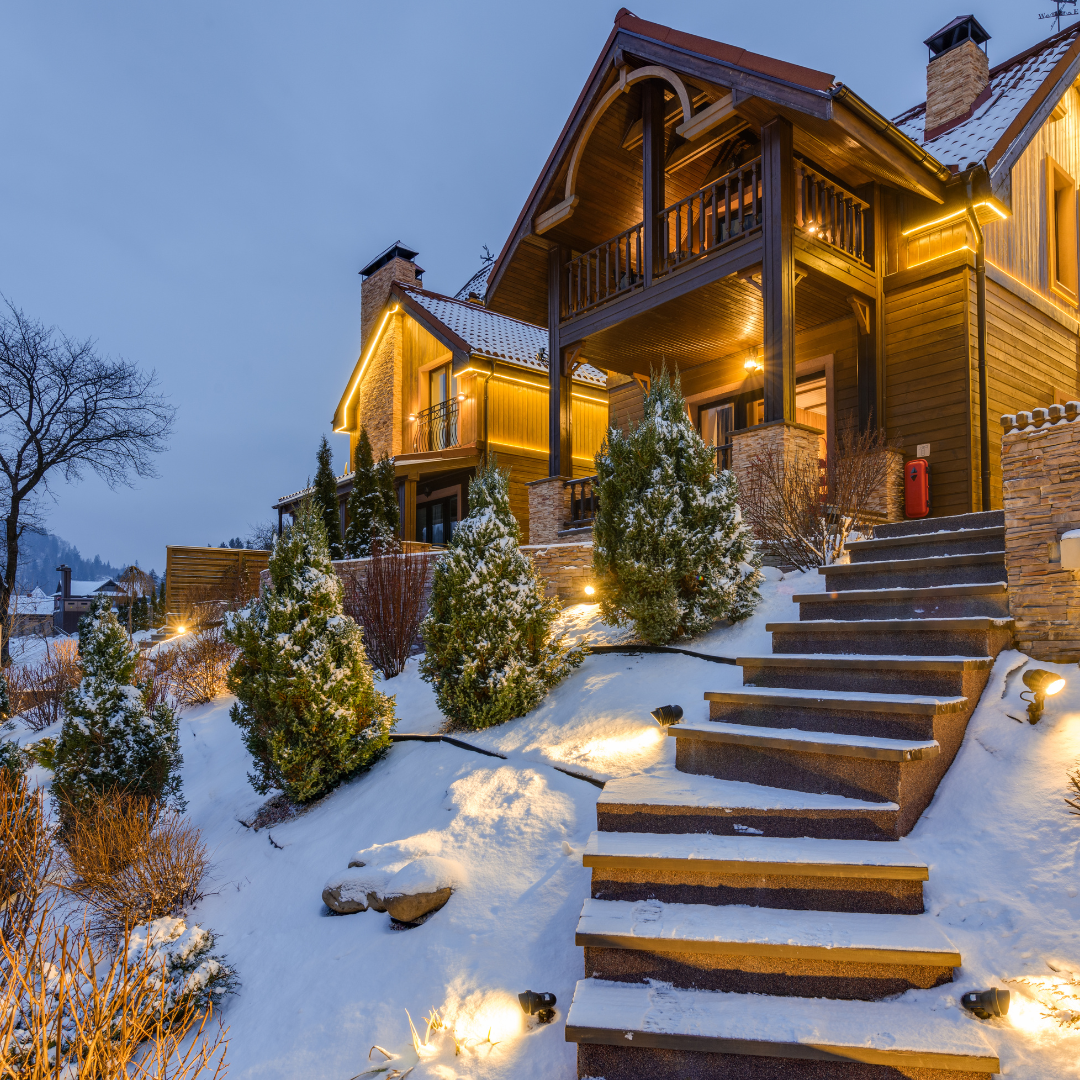 Rustic wooden chalet with outdoor lighting in a snowy landscape.